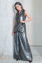 Load image into Gallery viewer, A woman wearing a sleeveless, double-breasted, grey shiny vest with front pockets, paired with tailored pants.