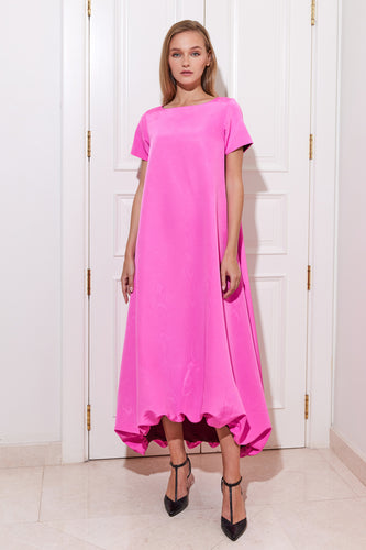A model wearing a pink moiré a-line dress with maroon lining and short sleeves, standing in front of a door.