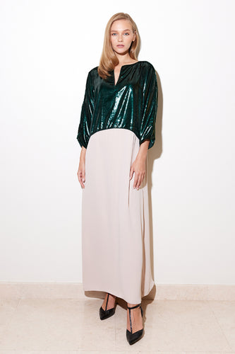 A model wearing a shiny emerald green lamé upper part with a nude crepe lower part dress, with a comfortable and elegant kaftan cut, side slits, and a front chest opening.