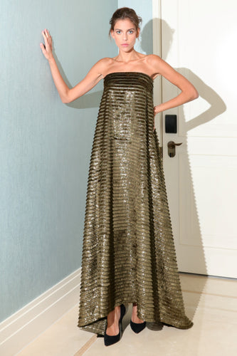 A woman wearing a vintage gold colored, fringed, straight-cut dress with a sweetheart neckline and three-quarter sleeves, standing in a room with a blue wall and white furniture.