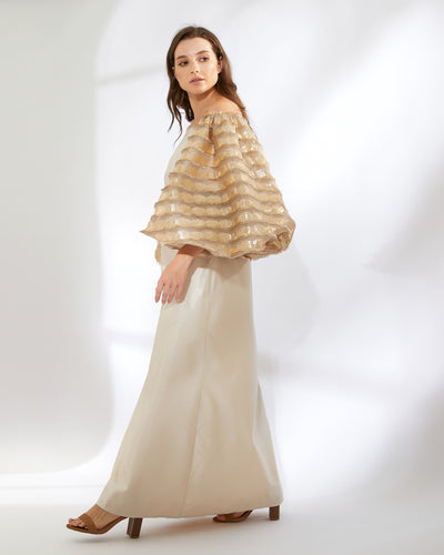 A woman wearing an off-shoulder dress with balloon shaped sleeves made of gold fil Coupe fabric with fringed threads, over a plain satin taffeta body.