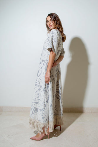 A woman wearing a textured grey and cream jacquard dress with palm leaves pattern, half sleeves, side pockets, and a cream fringed rope tassel edge.